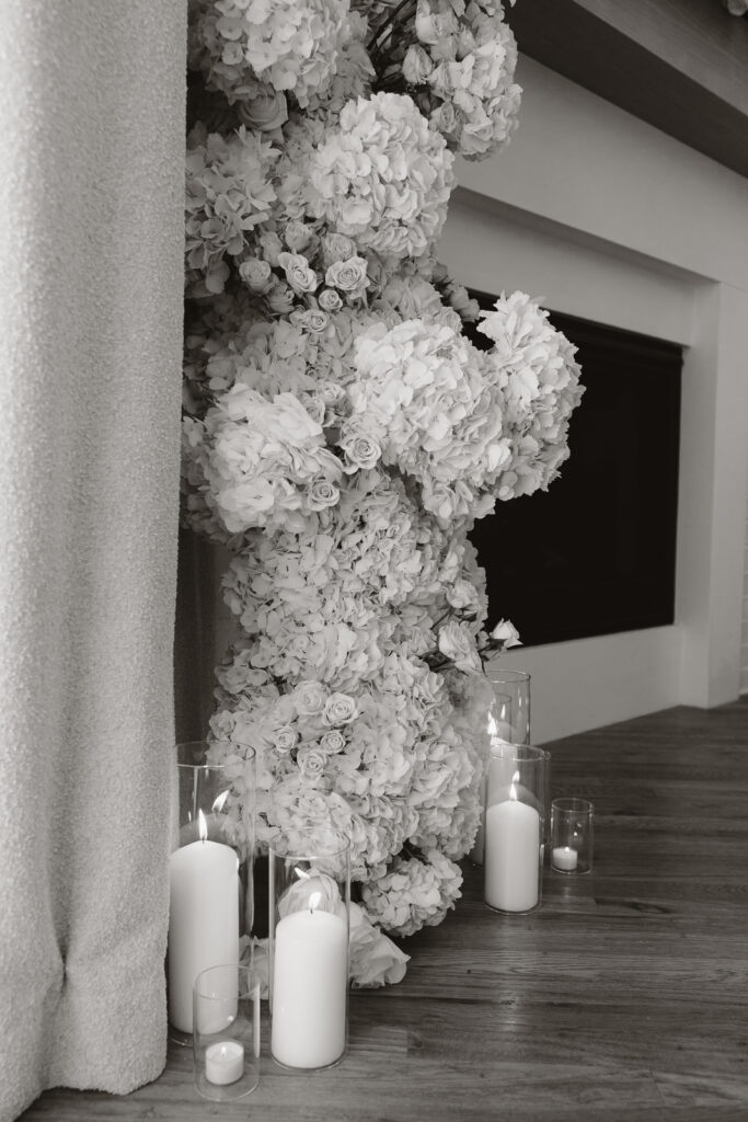 Simple, white candles line the base of a white flower arch in a modern white aesthetic home Timeless indoor wedding in Dallas, captured with a refined, editorial approach.