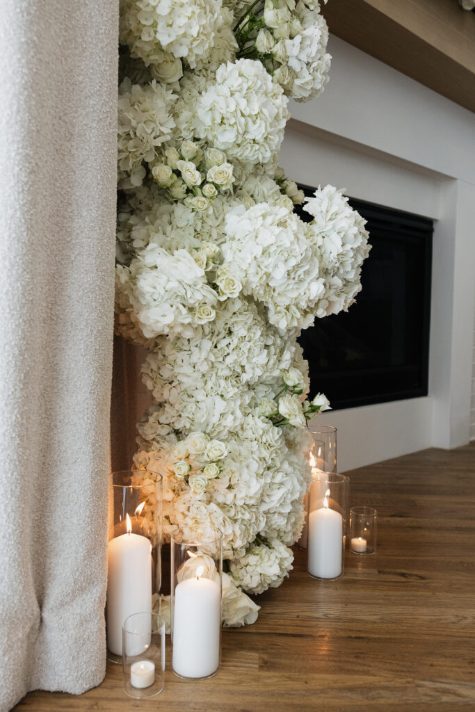 Simple, white candles line the base of a white flower arch in a modern white aesthetic home Timeless indoor wedding in Dallas, captured with a refined, editorial approach.