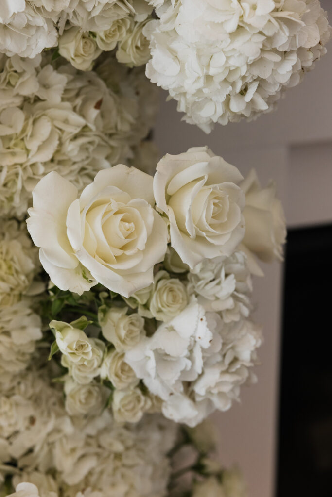 Simple, white flowers line the base of a white flower arch in a modern white aesthetic home for a wedding ceremony. Timeless indoor wedding in Dallas, captured with a refined, editorial approach by DFW documentary wedding photographer.