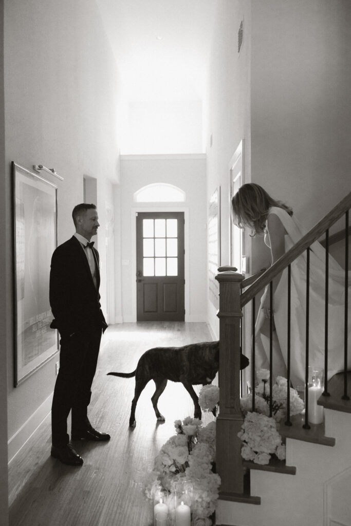 A groom looks affectionately at his bride as she walks down the stairs during their private first look. Timeless indoor wedding in Dallas, captured with a refined, editorial approach by DFW documentary wedding photographer.