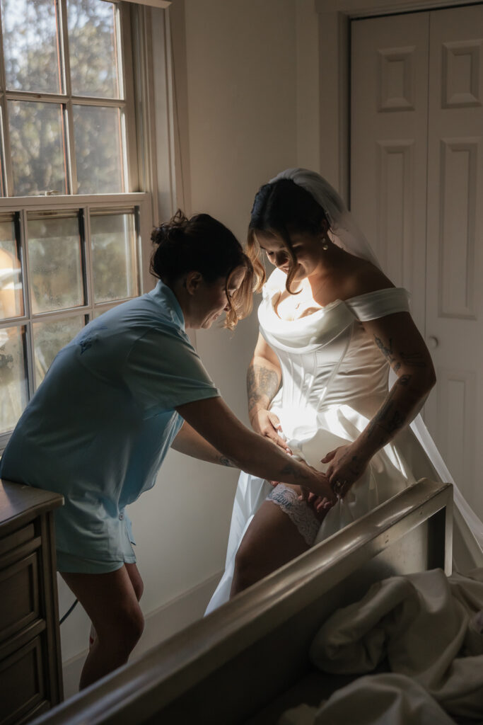 Bride getting ready, adjusting garter in sunny room.