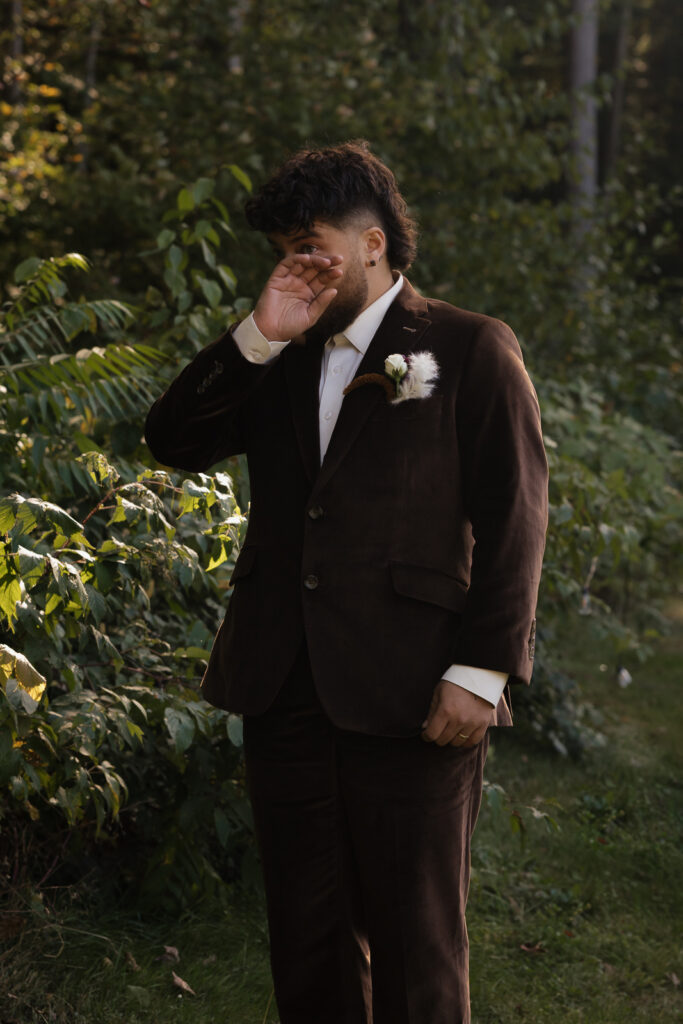 Man in a brown suit wiping tears in a garden