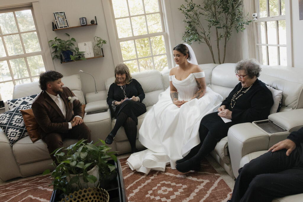 Bride in a white dress sitting on a couch with family members in a living room setting.