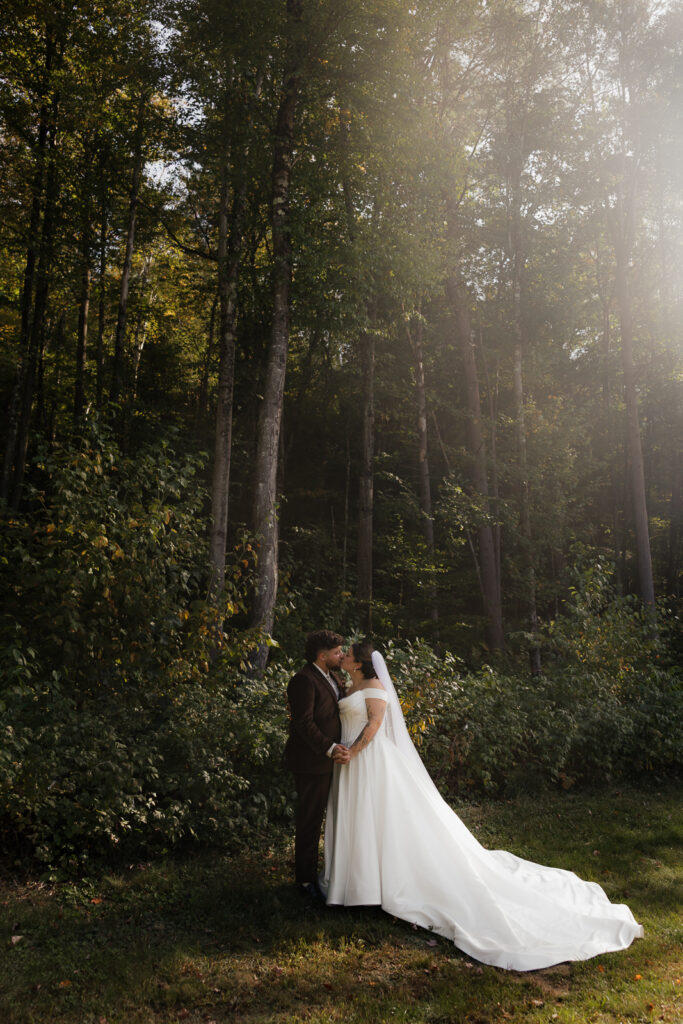 Bride and groom in wedding attire embracing in a forest setting.