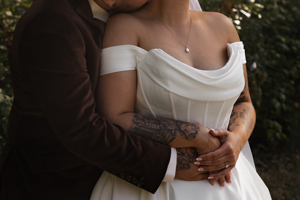 Close-up of a couple embracing, showing a wedding dress and tattoos.