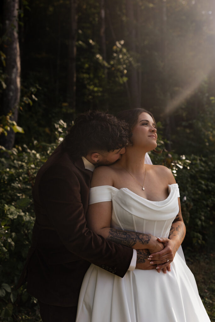 Bride in white dress embraced by groom in forest setting
