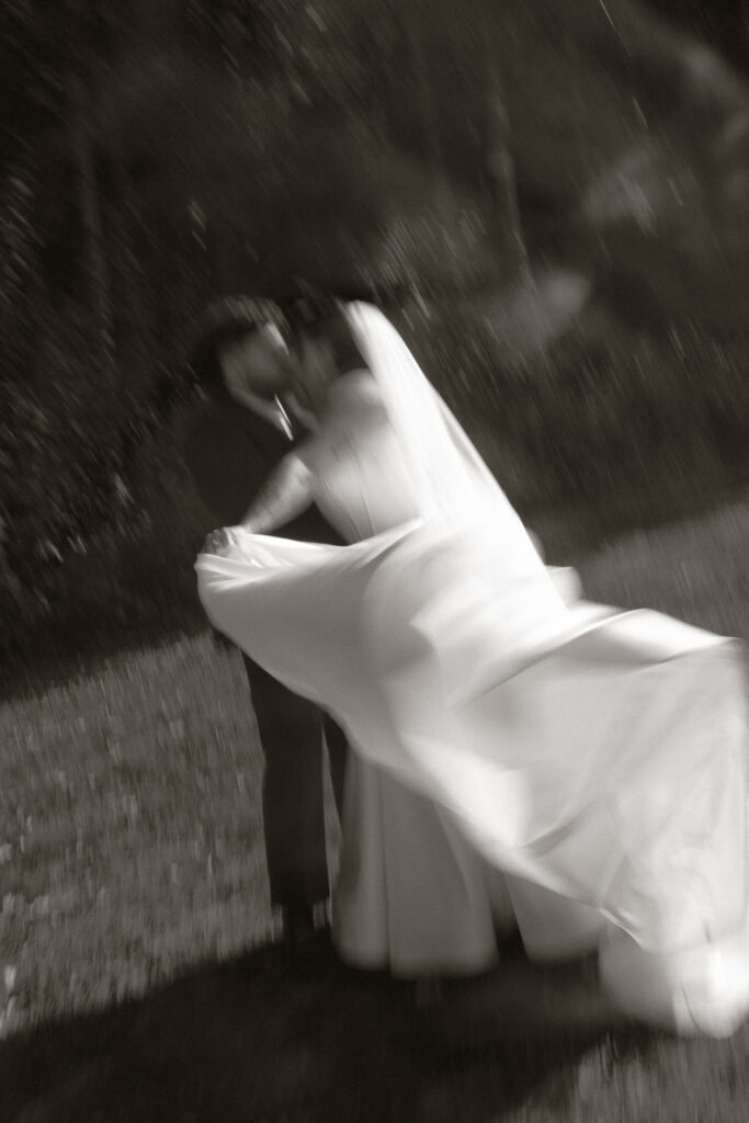 A blurred black and white photo of a couple kissing, with a flowing wedding dress creating soft movement.