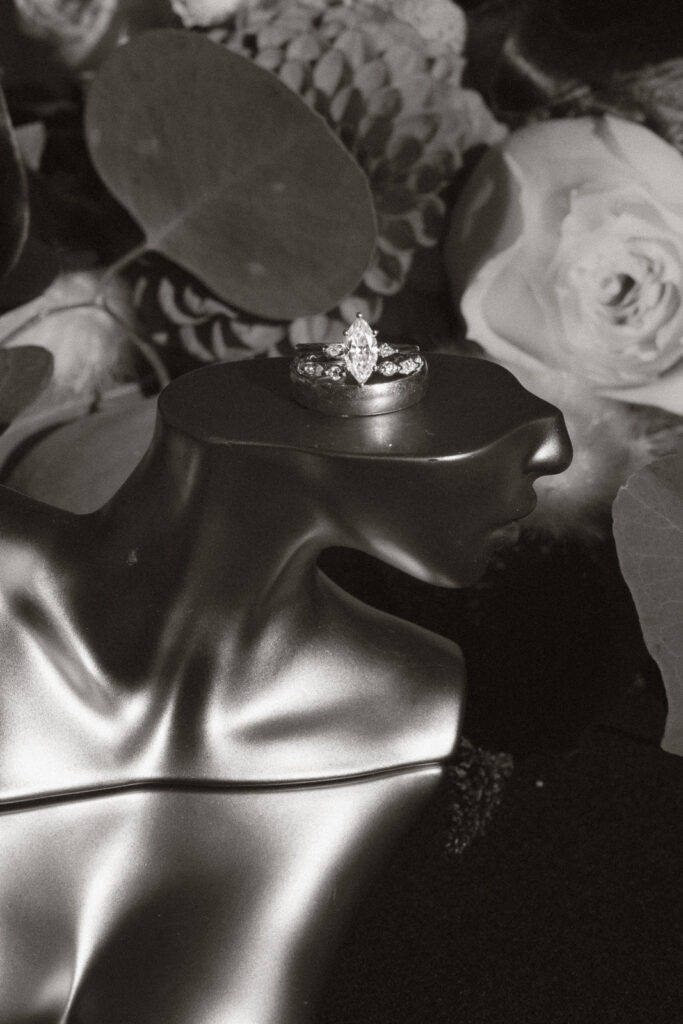 Silver ring with a marquise diamond on a black mannequin bust, surrounded by floral backdrop.