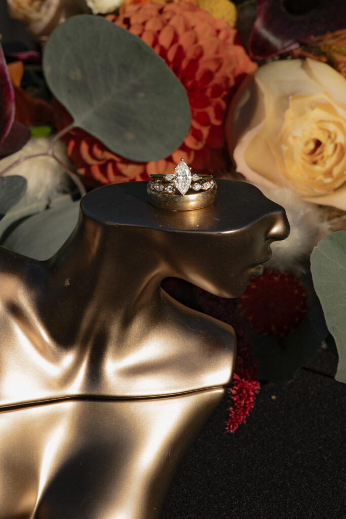 Elegant diamond ring on golden mannequin bust with flower background