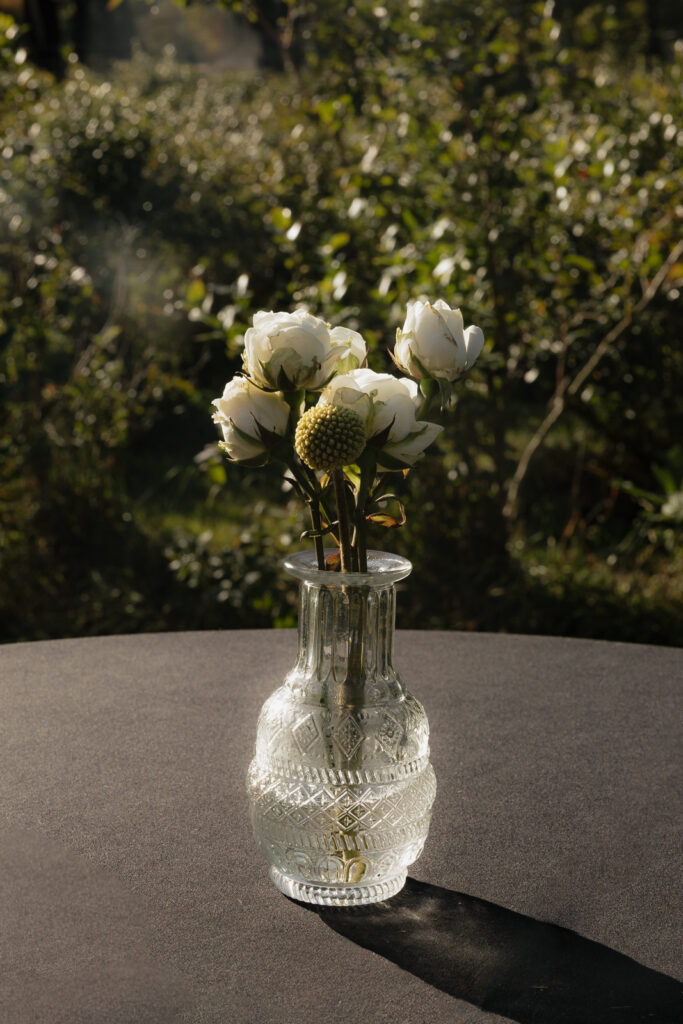 White flowers in a textured glass vase on an outdoor table.
