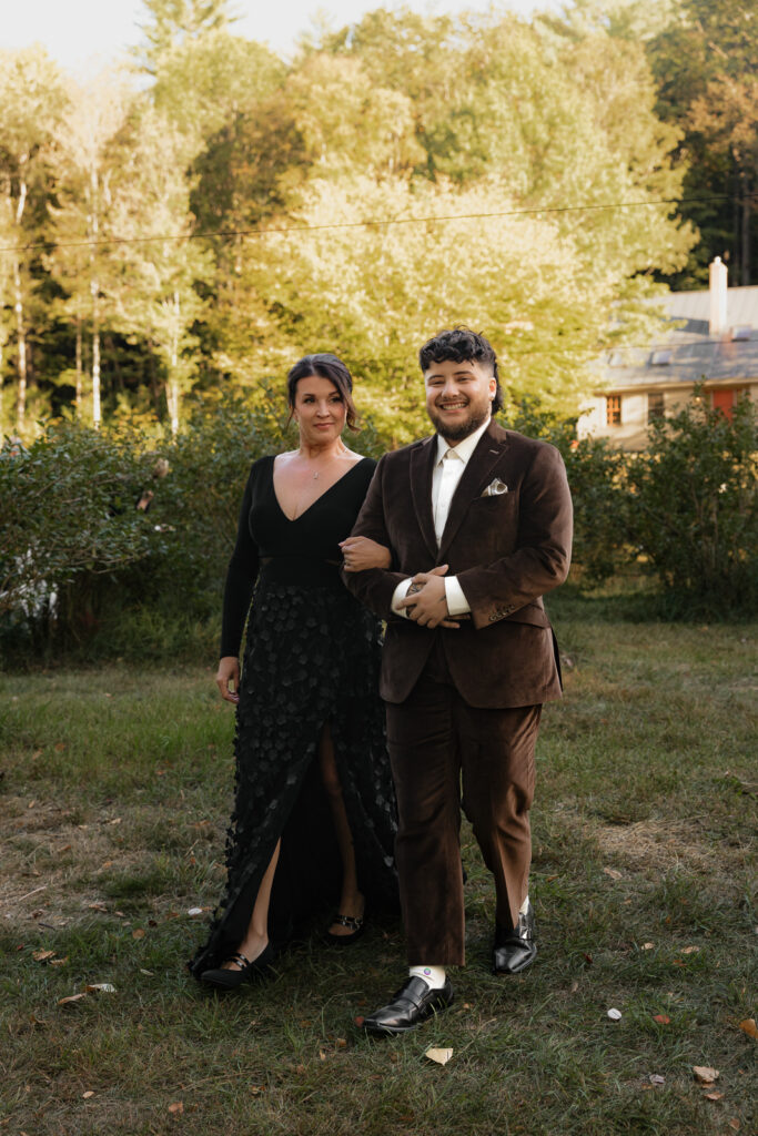 A man and woman dressed elegantly walking on grass with trees in the background.
