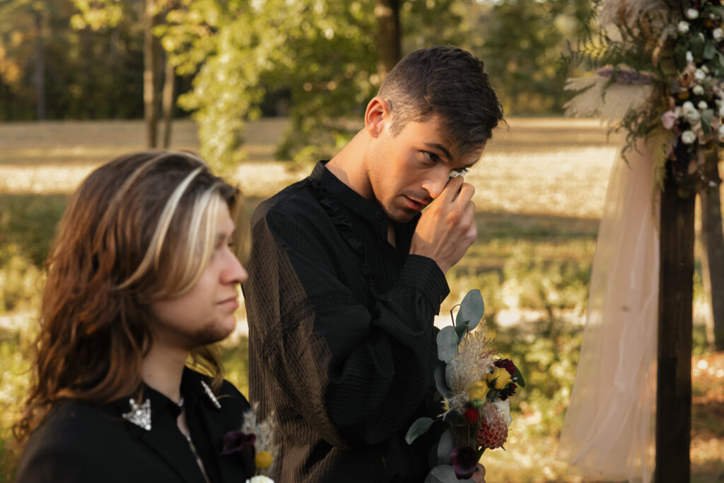 Emotional groom wiping tears during outdoor wedding ceremony