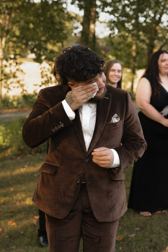 Person in brown suit wiping tears at outdoor event