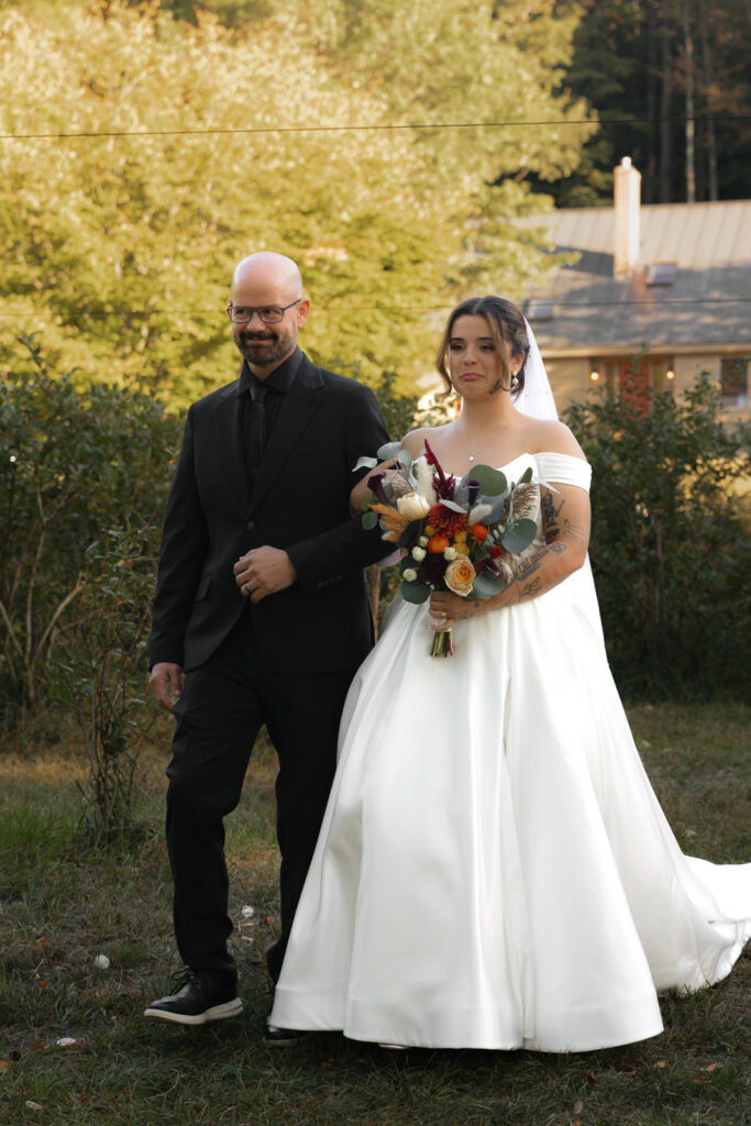 Bride in a white gown walking with a man in a black suit, outdoor setting