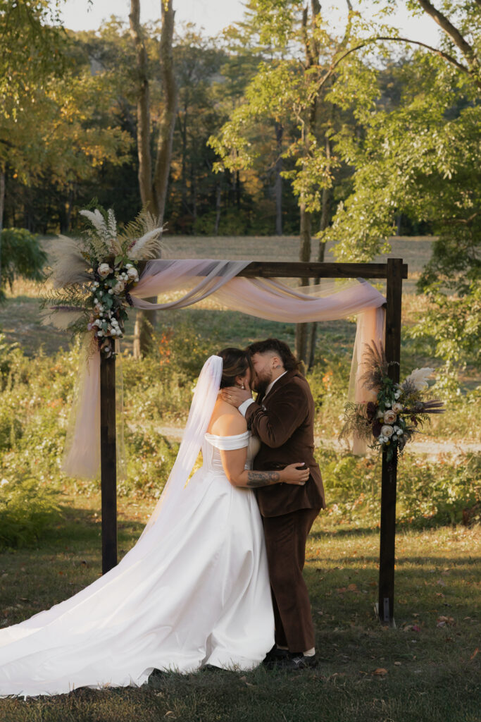 Bride and groom kiss under rustic arch outdoors