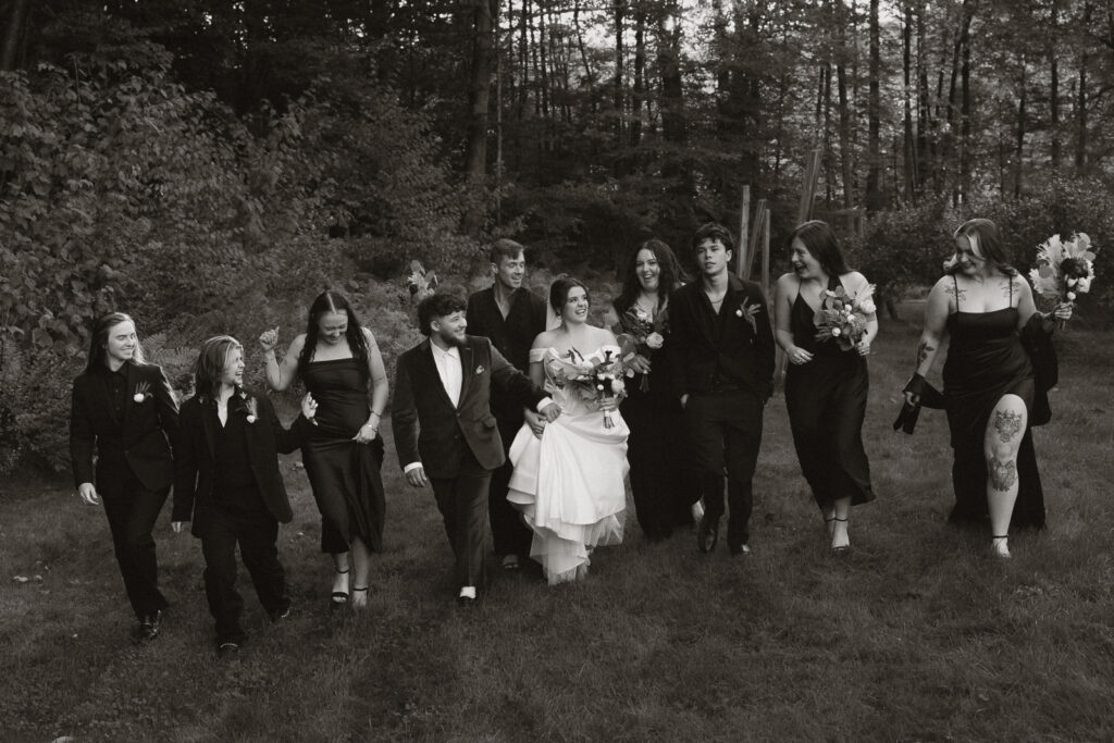 Black and white photo of a wedding party walking outdoors in a forested area.