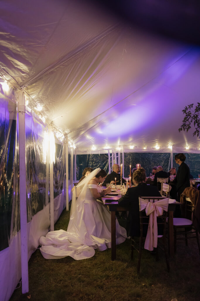 Bride in a white gown seated inside a decorated tent at night.