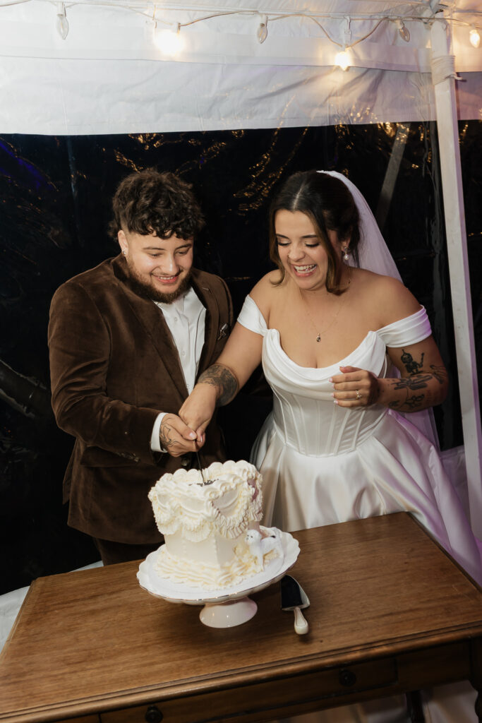 Bride and groom cutting wedding cake under string lights