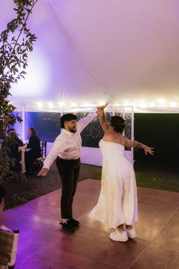 A couple dancing under a tent with string lights at night, wearing formal attire.