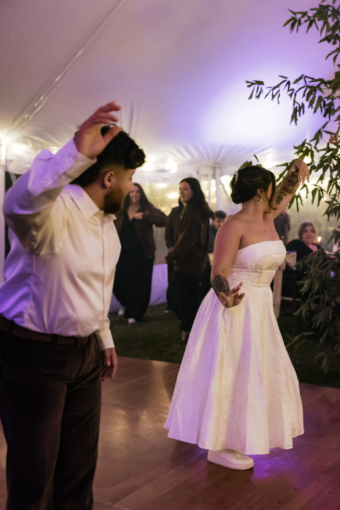Bride and groom dancing at a wedding reception under a tent with purple lighting.