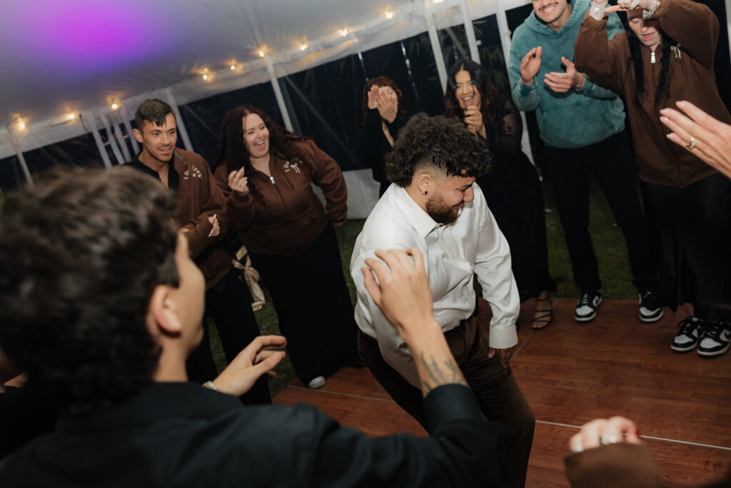 Group of people dancing at a lively event under a tent with string lights.