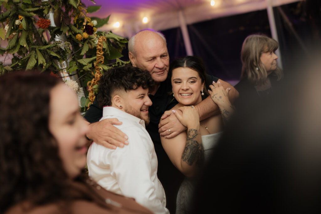 Group of people smiling and embracing at a celebration with floral decorations in the background.