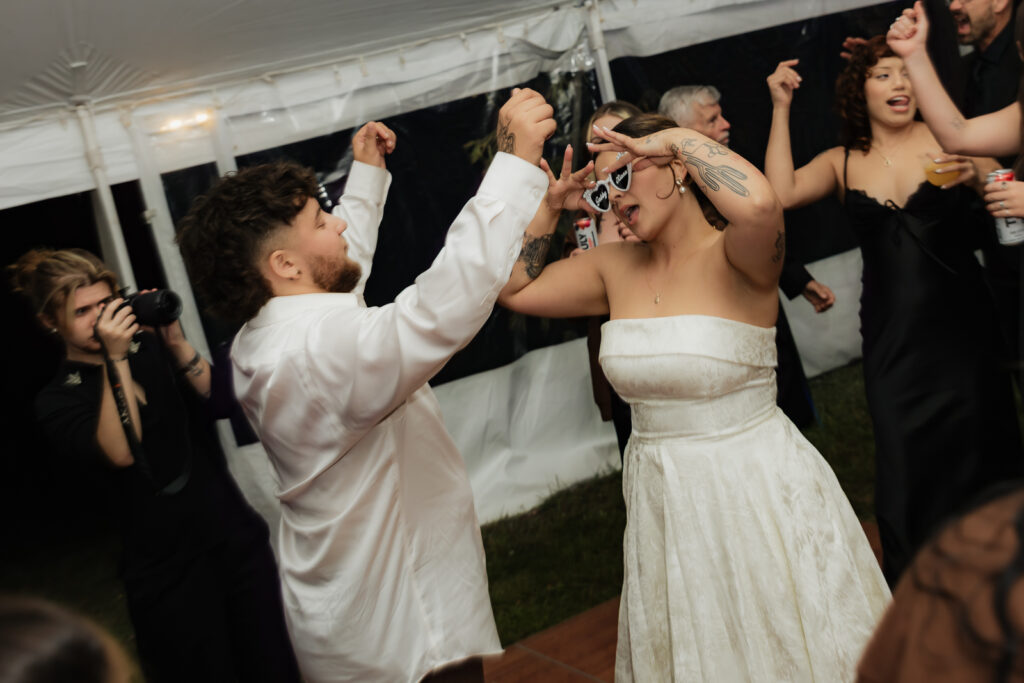People dancing and celebrating at a wedding reception under a tent.