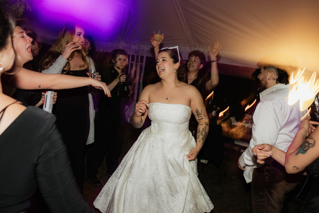 Bride dancing at a lively party with friends under colorful lights.