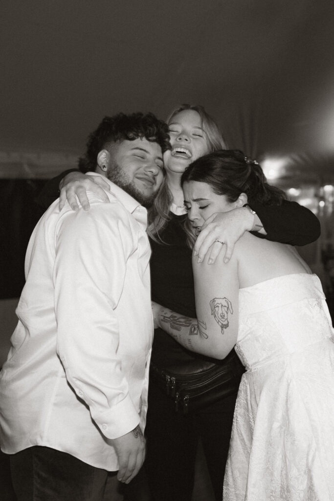 Three people embracing closely in a joyful moment, with one wearing a white dress.