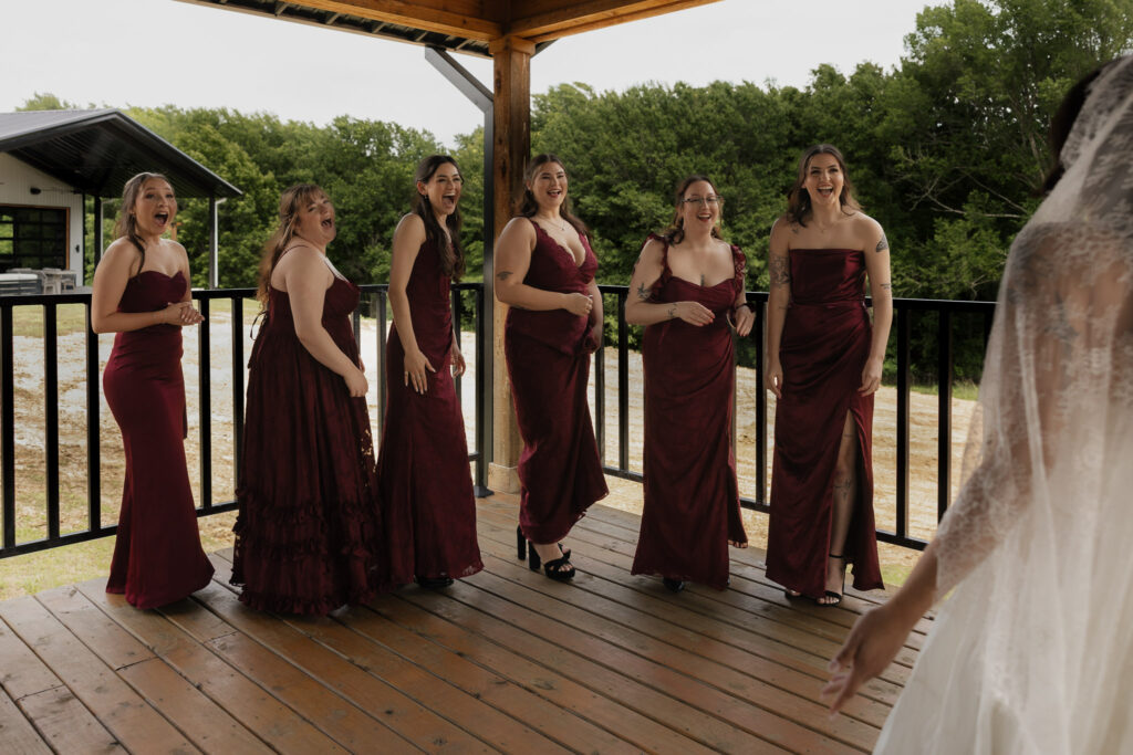Bridesmaids in burgundy dresses react to bride
