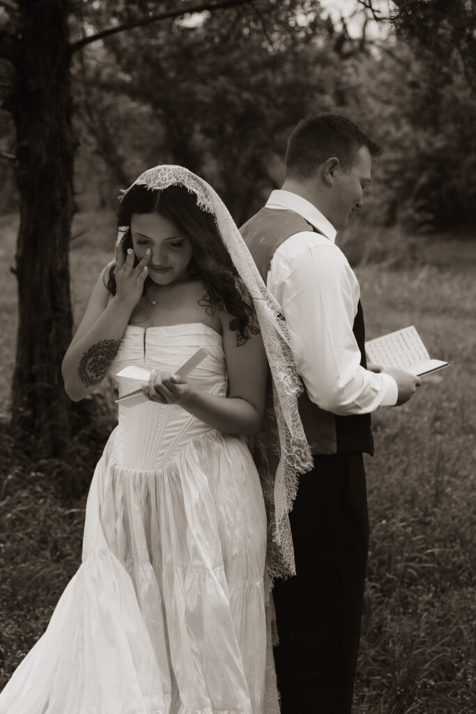 Bride and groom reading letters back to back outdoors.