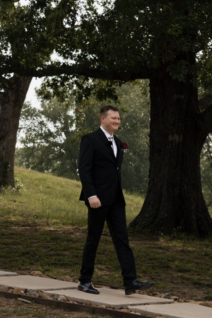 Man in black suit walking along a path under trees