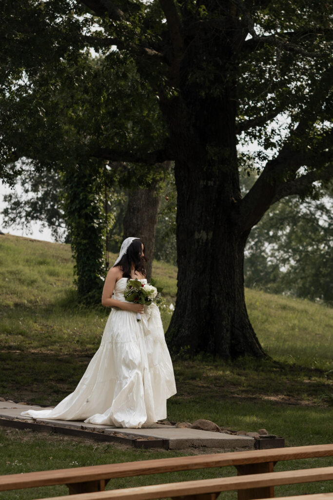 Bride in white gown walking outdoors with greenery background