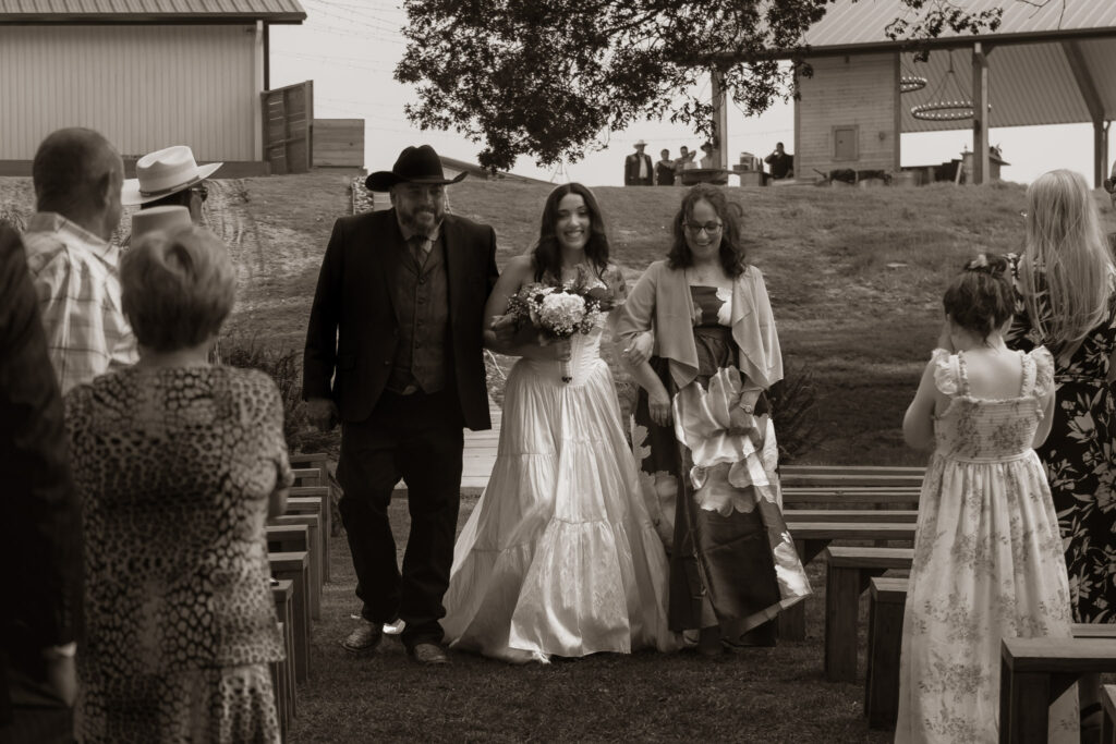 Bride walking down the aisle with two companions outdoors.