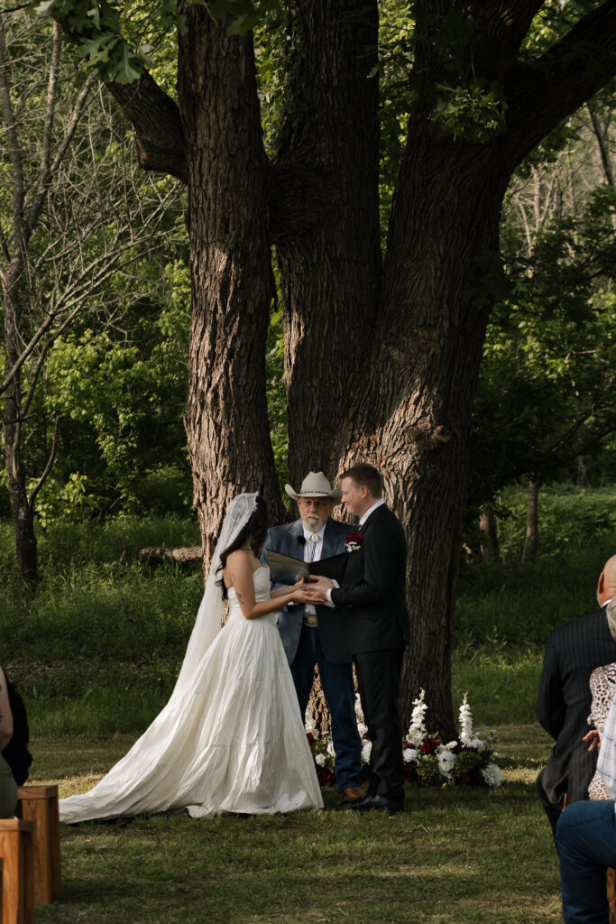 Bride and groom exchange vows outdoors under a large tree