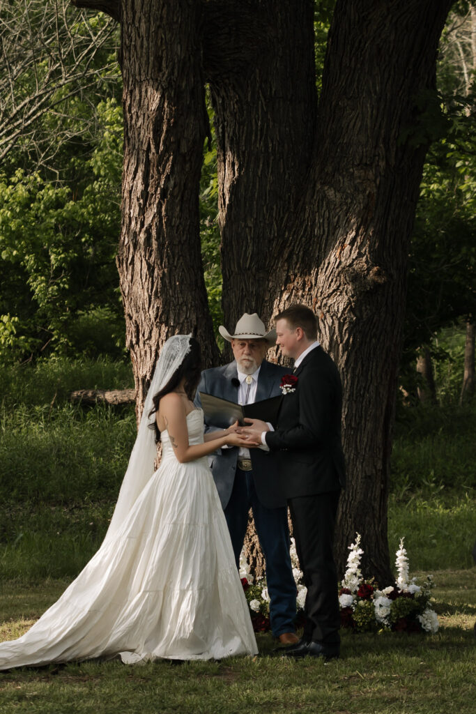 Wedding couple exchanging vows under tree outdoors