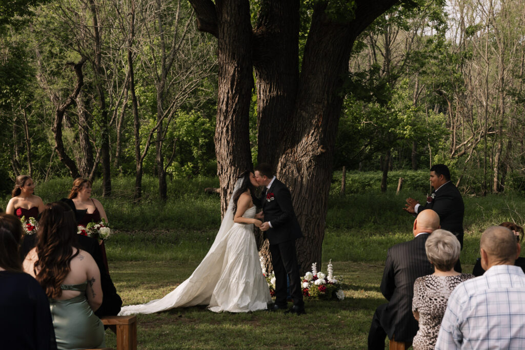 Outdoor wedding ceremony with bride and groom kissing under a tree