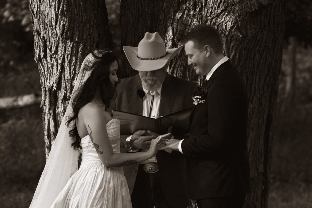 Bride and groom exchange vows outdoors with officiant in cowboy hat