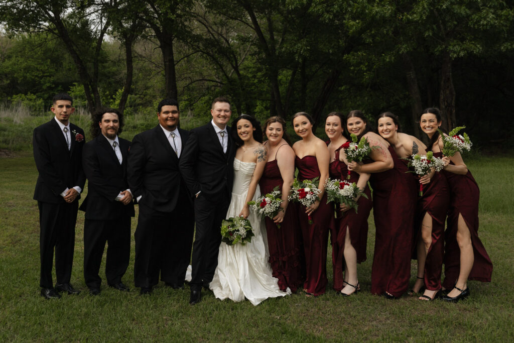 Wedding party posing outdoors with smiling bridesmaids and groomsmen.