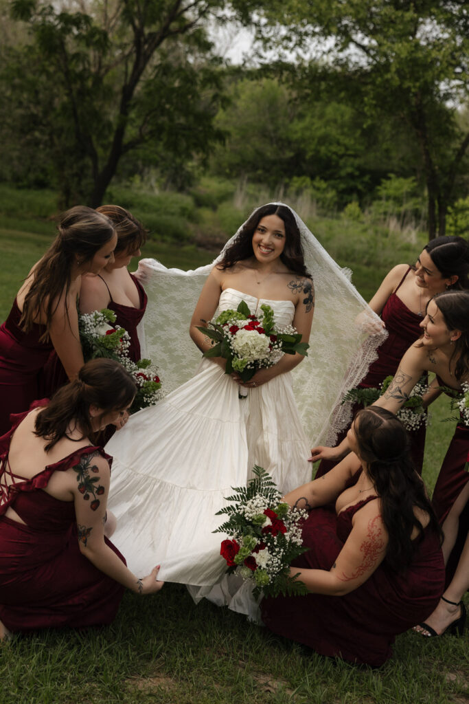 Bride surrounded by bridesmaids in burgundy dresses outdoors