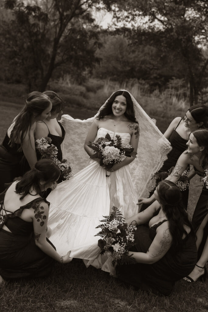 Bride surrounded by bridesmaids with tattoos holding bouquets in a sepia-toned photo.