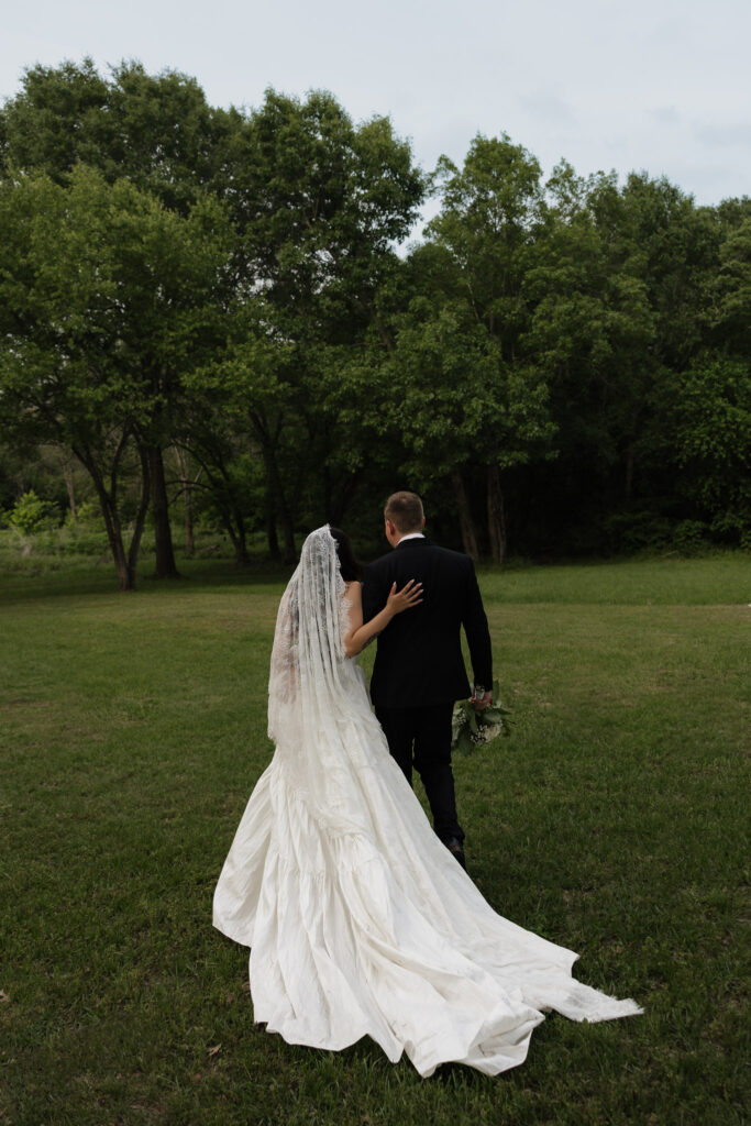 Bride and groom walking in a lush green field.