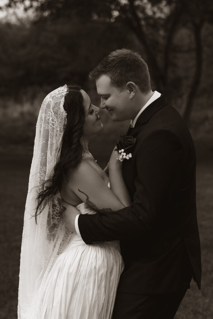 Bride and groom smiling at each other outdoors in wedding attire