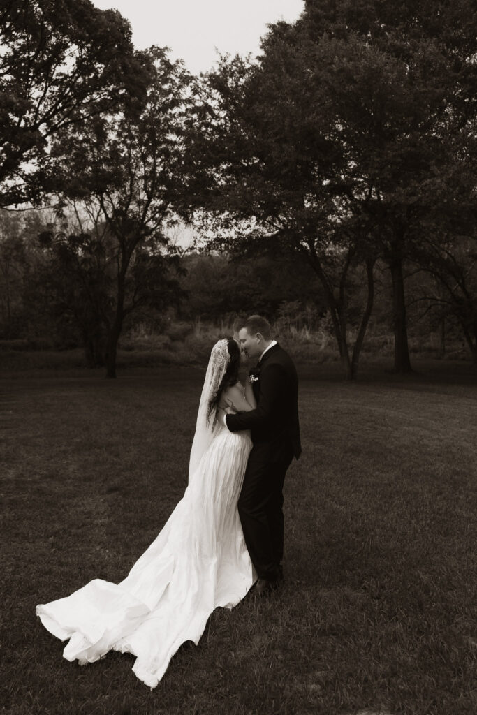 Bride and groom embrace in an outdoor setting with trees