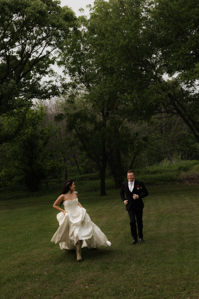 Bride and groom running in a grassy field with trees in the background