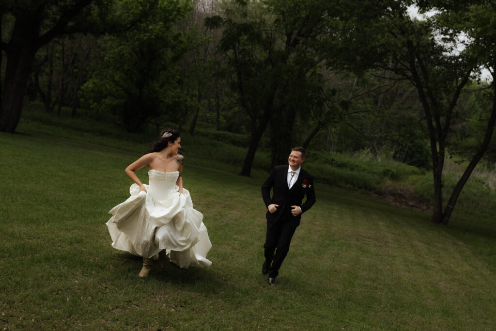 Bride and groom joyfully running in a lush green park.