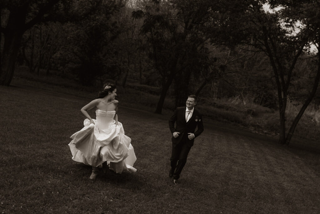 Bride and groom running happily in a grassy field.
