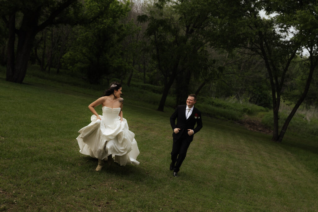 Bride and groom running joyfully on a lush green lawn surrounded by trees