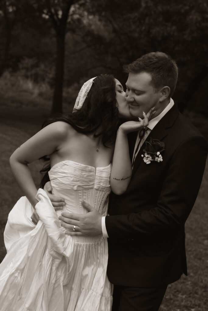 Bride and groom share a romantic kiss outdoors.