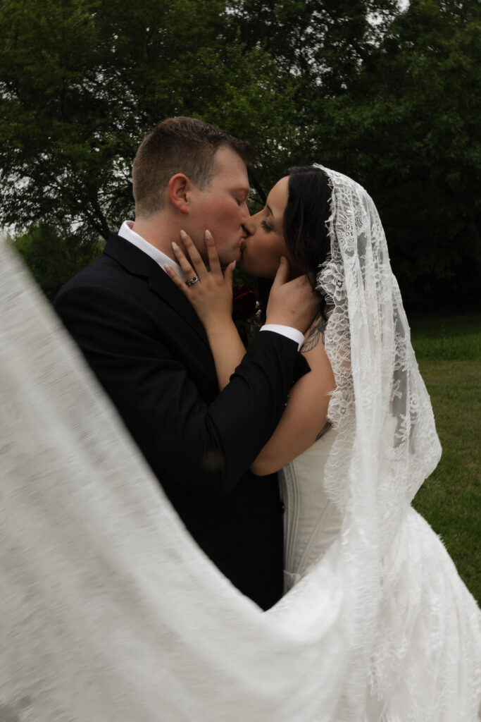 Bride and groom sharing a romantic kiss outdoors.